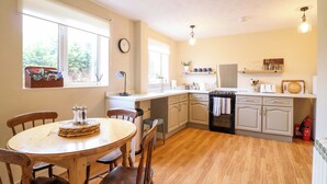 A kitchen with wooden cabinets, a dining table with chairs, a clock, and a window with blinds. - 2 Horseshoe Road (Montgomery)