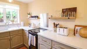 A kitchen with a stove, oven, sink, and a window with a view of greenery. There are shelves with glassware and a plant on the windowsill. - 2 Horseshoe Road (Montgomery)
