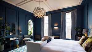 A bedroom with a large bed, a desk, a chair, and a hanging light fixture.