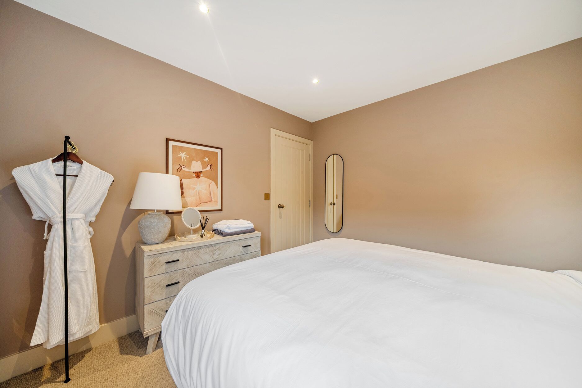 A bedroom with a bed, a dresser, a robe, a lamp, and a mirror.