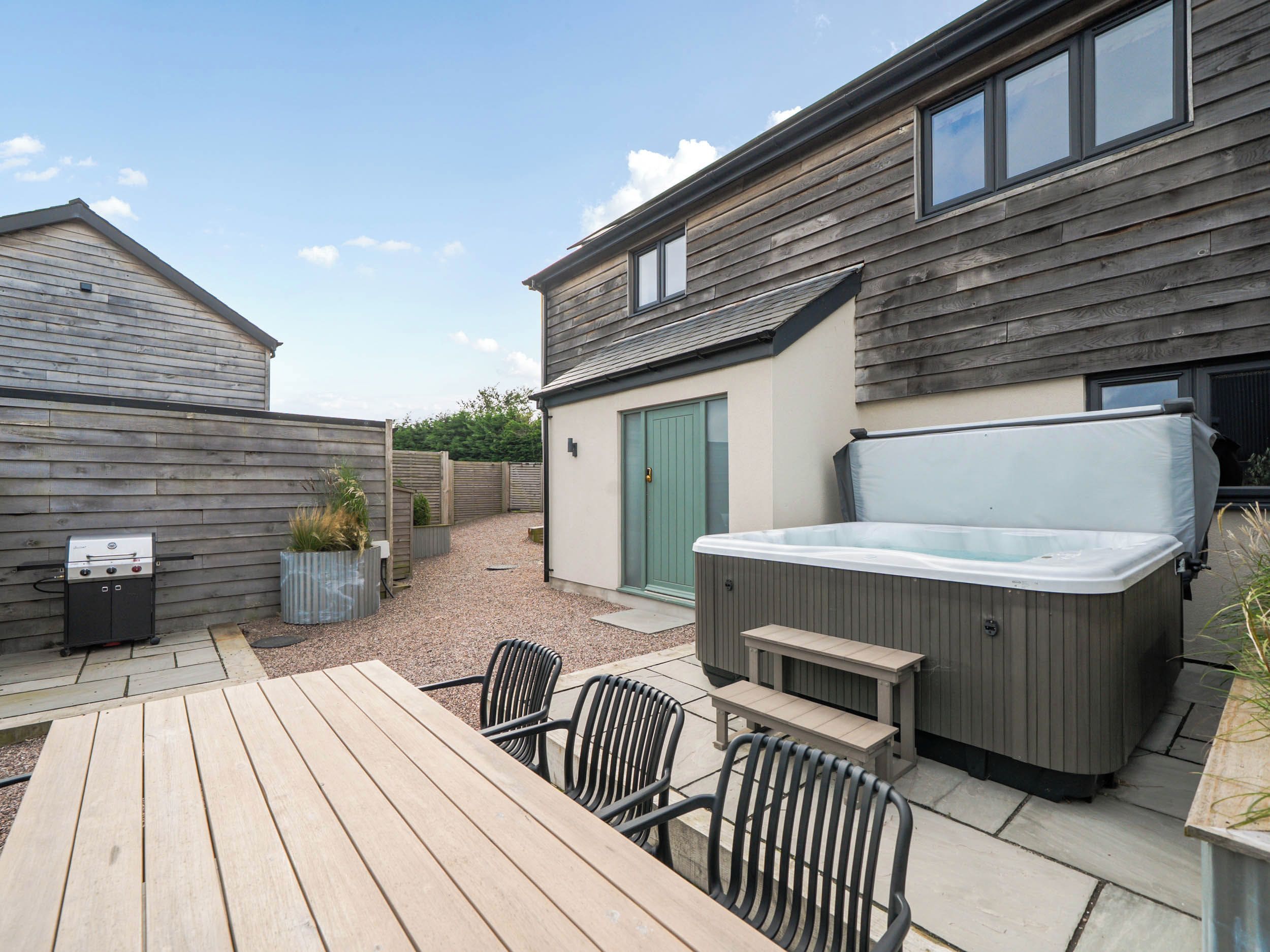A patio area with a wooden table and chairs, a hot tub, and a barbecue grill.