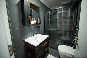 A modern bathroom with a white sink, dark tiles, a glass shower enclosure, and a wooden vanity. - ASİL VİLLA SAPANCA (Sapanca)
