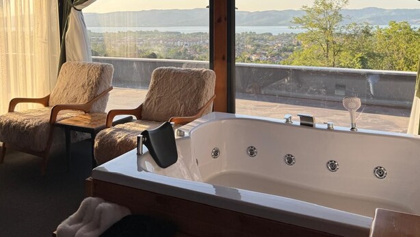 A bathroom with a bathtub, two chairs, and a view of a lake and mountains. - ASİL VİLLA SAPANCA (Sapanca)
