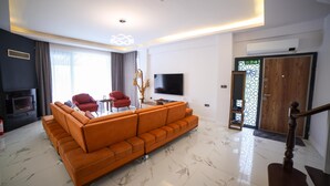 A modern living room with a large orange sofa, a flat-screen TV, and a fireplace. - ASİL VİLLA SAPANCA (Sapanca)