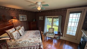 Une chambre à coucher comprenant un lit, une chaise, un bureau, un ventilateur de plafond et une grande fenêtre donnant sur l’extérieur.