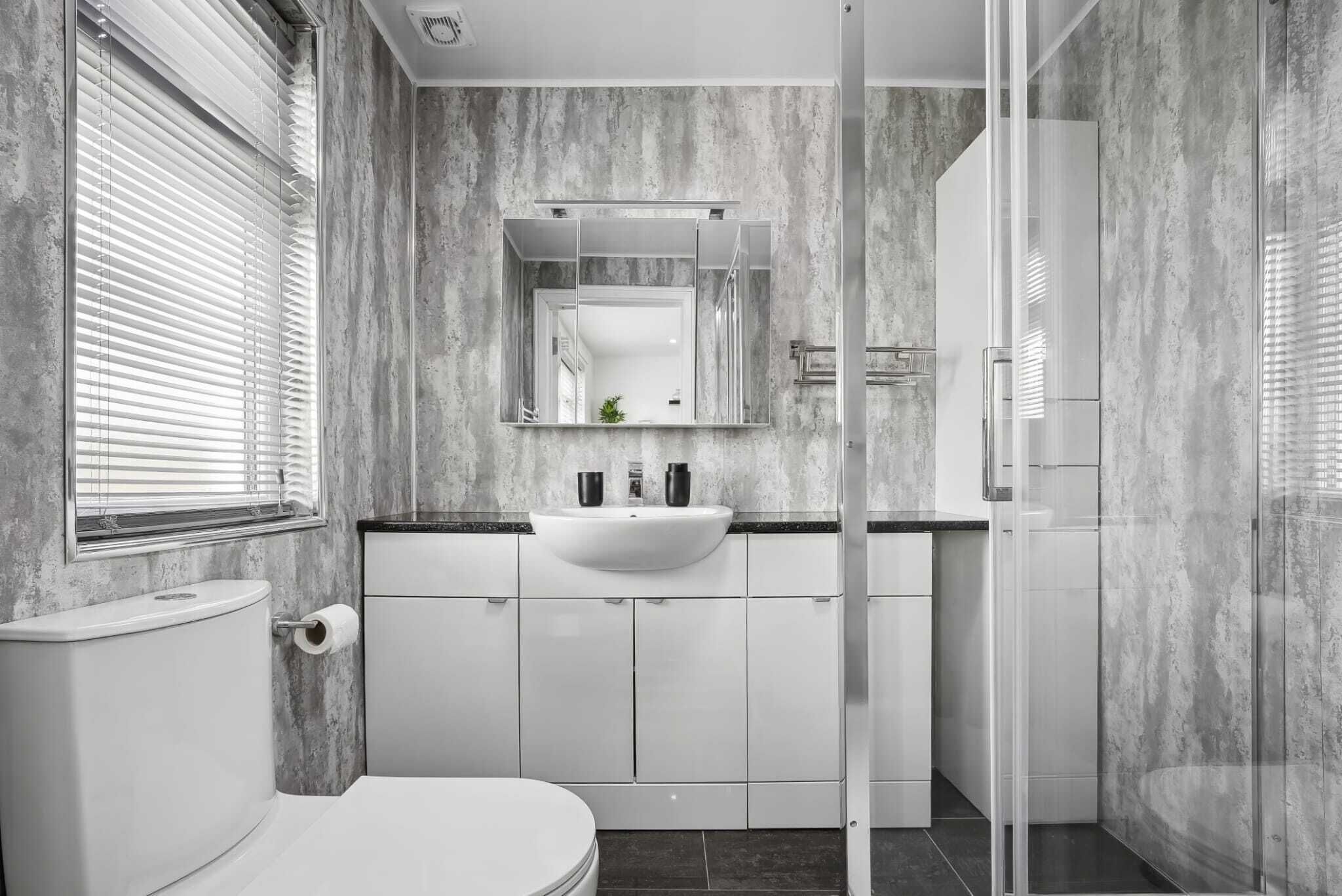 A modern bathroom with a marble wall, a white sink, and a glass shower enclosure.