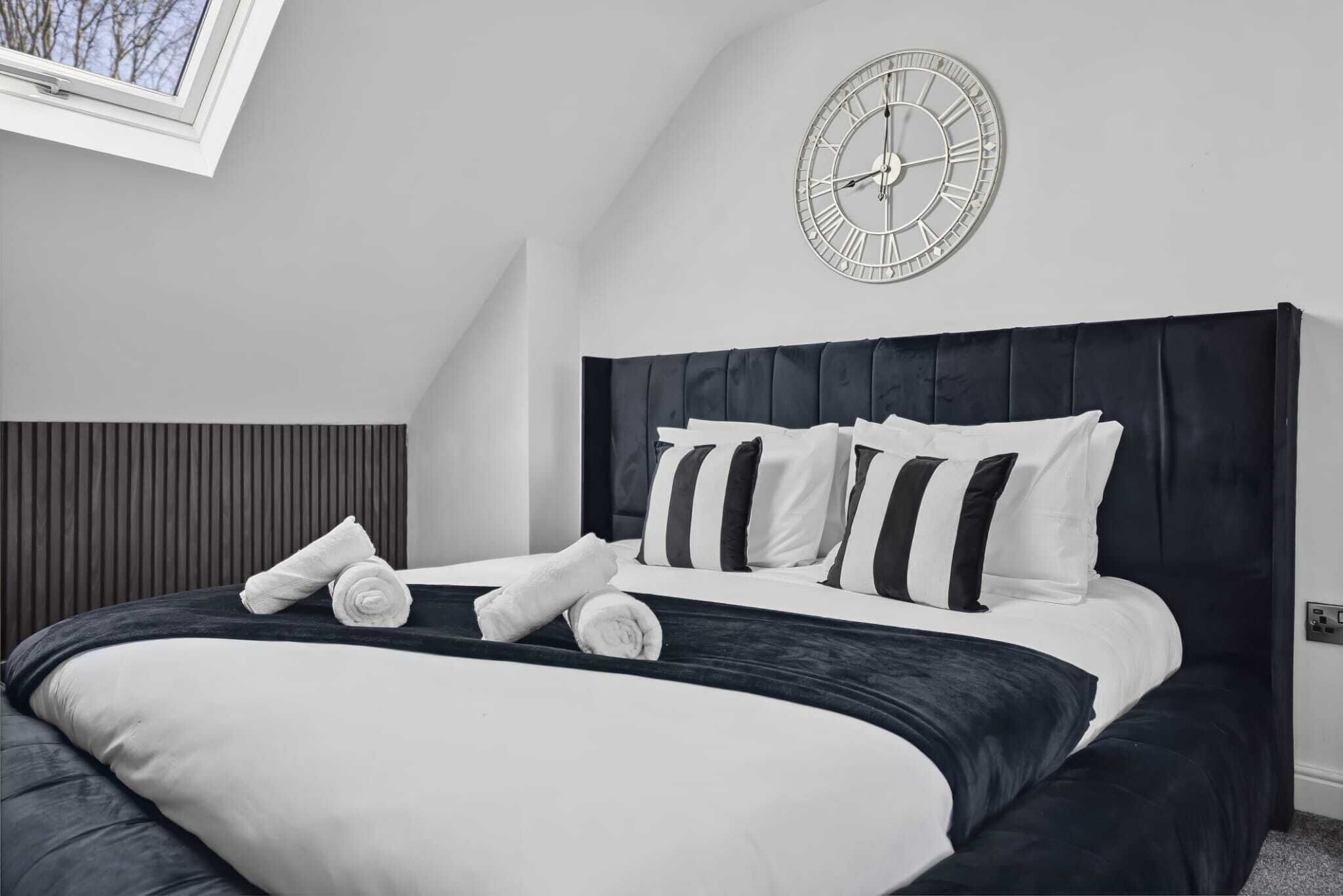 Un dormitorio con una cama grande, un reloj en la pared y una ventana con vista a árboles.