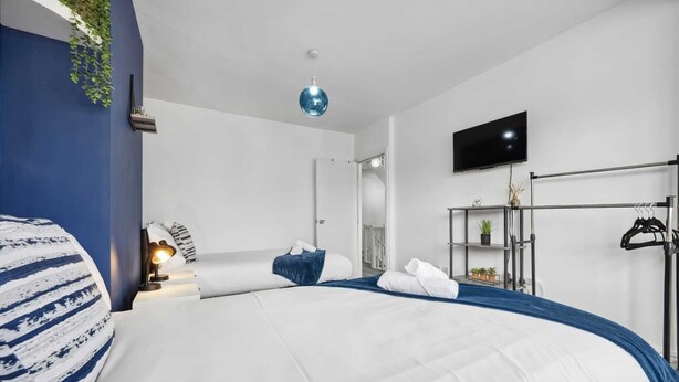 A modern hotel room with a large bed, a TV mounted on the wall, a wardrobe, and a small plant on the shelf.