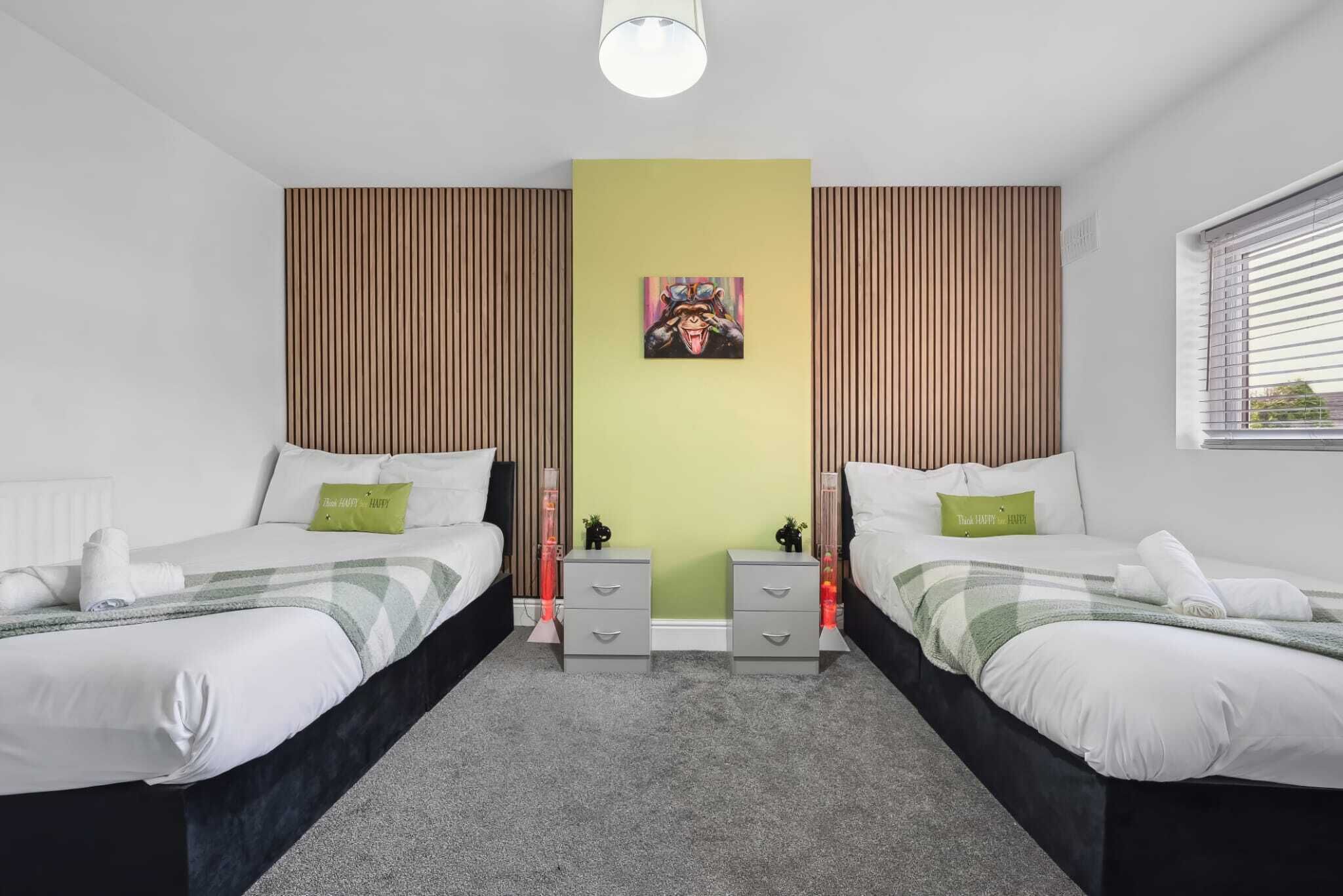A modern bedroom with two beds, a green accent wall, and a painting.