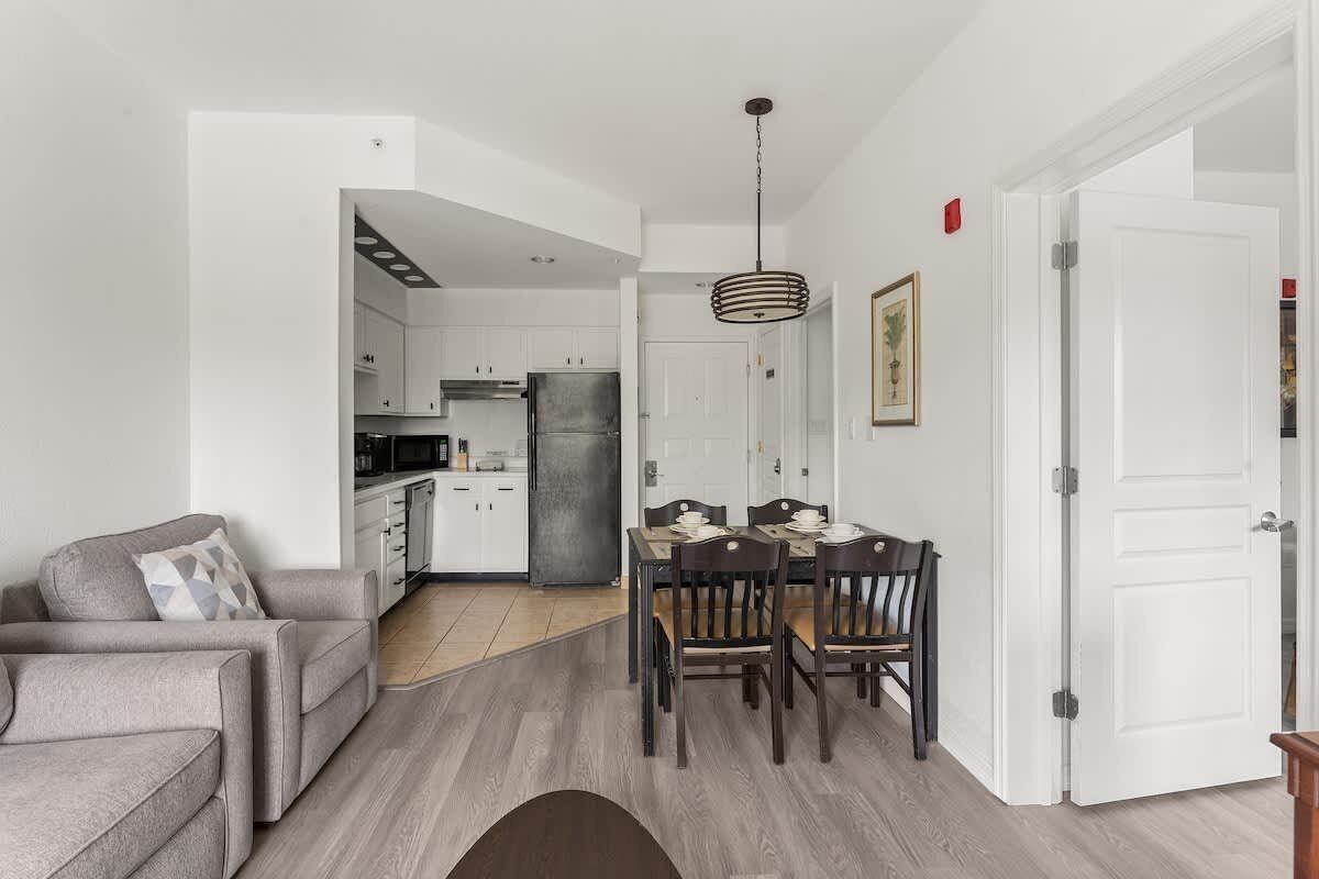 A modern kitchen with white cabinets, a stainless steel refrigerator, and a dining area with a wooden table and chairs.
