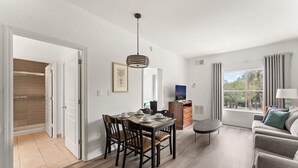 Una sala moderna con comedor, un sofá, un televisor y una ventana con cortinas.
