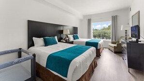 Habitación de hotel con dos camas, un escritorio, un televisor y una ventana con vista a zonas verdes.