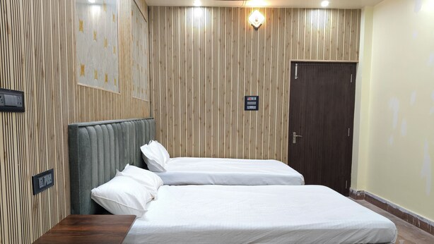A hotel room with two beds, a wooden wall panel, a door, and a small table. - The Royal Prince Hotel (Nawada)