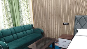 A room with a green sofa, a small wooden table, a nightstand with a drawer, and a bed with a grey headboard. - The Royal Prince Hotel (Nawada)