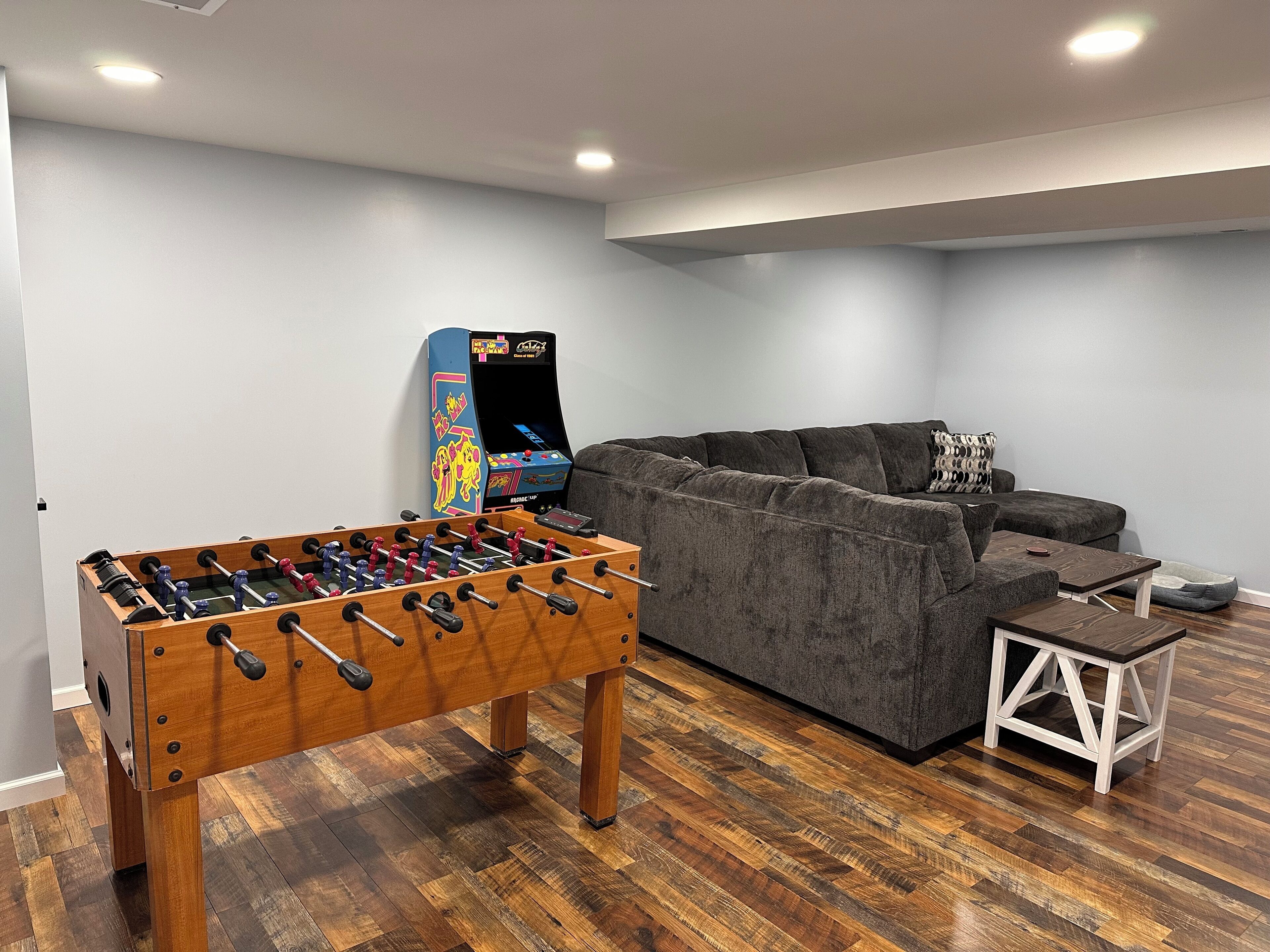 Ein Zimmer mit einem Kicker, einem grauen Sofa und einem kleinen weißen Tisch.