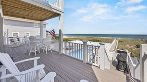 Une terrasse en bois avec des chaises blanches et une piscine, donnant sur la plage.