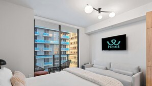 Een moderne hotelkamer met een bed, een bank, een televisie en uitzicht op een blauw gebouw.
