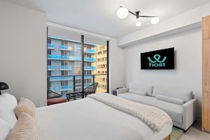 Une chambre d’hôtel moderne équipée d’un lit, d’un canapé, d’une télévision et offrant une vue sur un immeuble bleu.