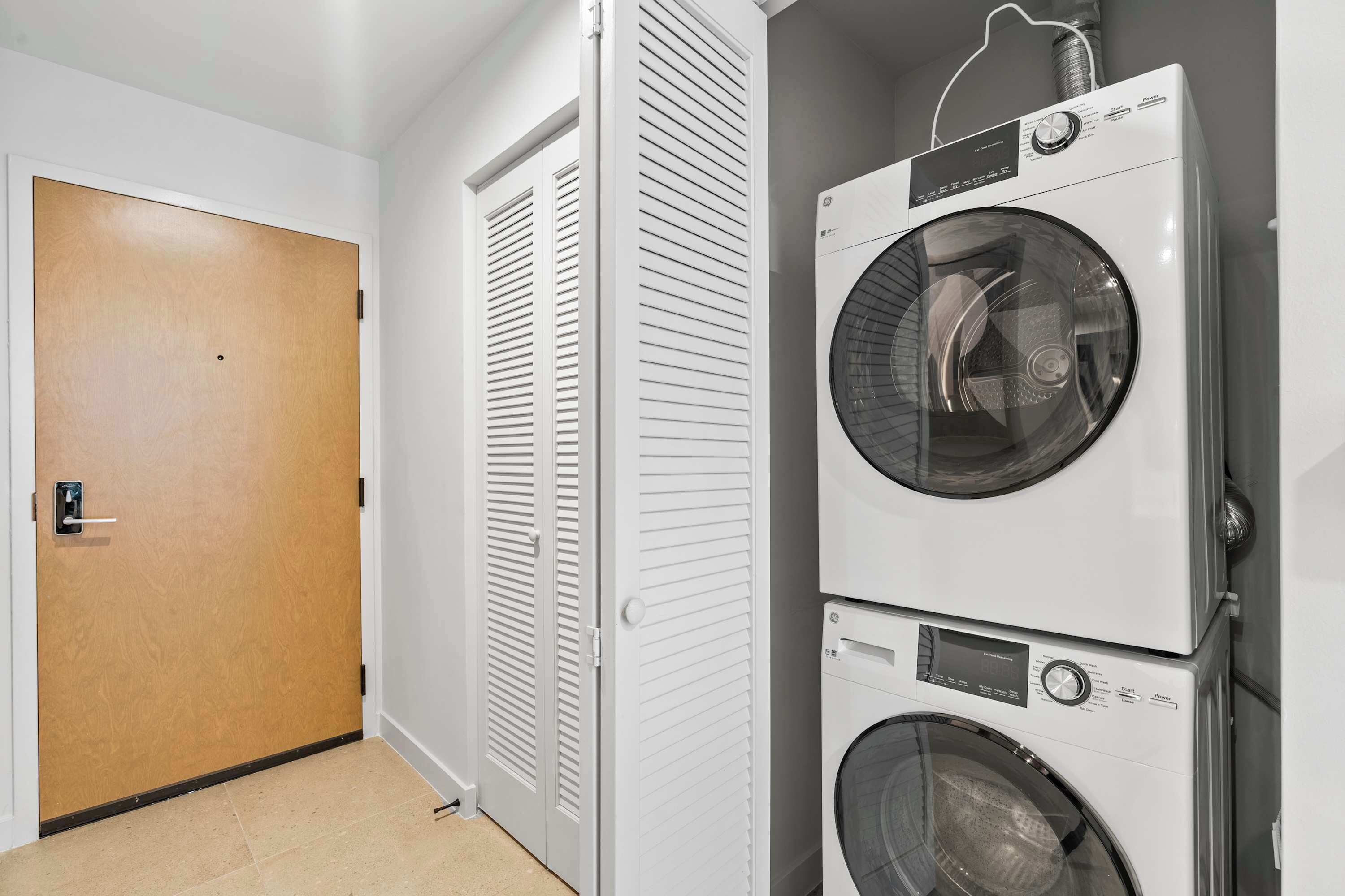 A laundry room with two stacked front-loading washing machines and a wooden door.