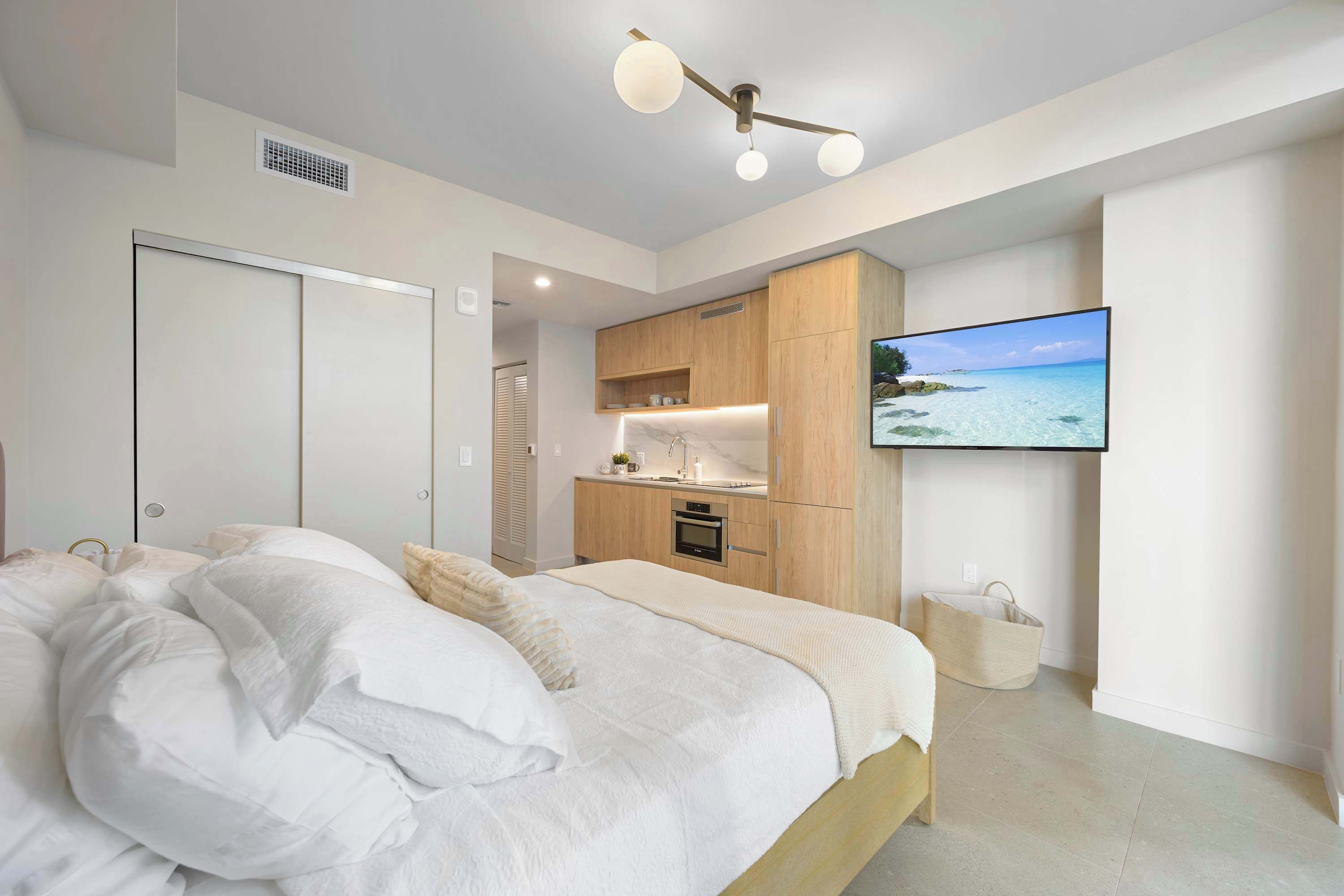 A modern bedroom with a large bed, a TV, and a kitchenette.