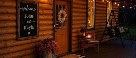 A wooden cabin with a porch, a welcome sign, a swing chair, and a lantern.