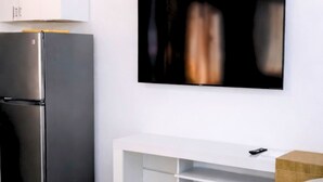 Ett modernt kök med ett kylskåp i rostfritt stål, en vit inbyggd ugn och ett vitt konsolbord med en glasskiva.
