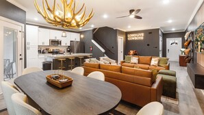 A modern kitchen with white cabinets, a large island, and a dining area with a dark wood table and chairs. - Modern 4BR Ensuite Townhome Near Texas A&M (College Station)