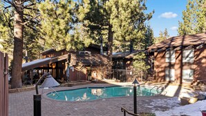 A pool area with a wooden deck, a hot tub, and a building with a balcony. - 2BR Overlooks Shared Pool, Near Gondola & Village! (Mammoth Lakes)