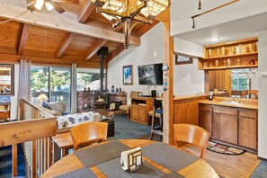 A cozy interior with a wooden dining table, chairs, a fireplace, and a kitchen area with wooden cabinets and a countertop. - 2BR Overlooks Shared Pool, Near Gondola & Village! (Mammoth Lakes)