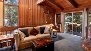 A cozy cabin interior with a wooden ceiling, a sofa with cushions, a small table, and a suitcase. - 2BR Overlooks Shared Pool, Near Gondola & Village! (Mammoth Lakes)