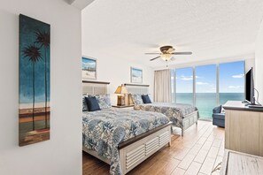 Ein Schlafzimmer mit zwei Betten, einem Deckenventilator, einem Fernseher und einem großen Fenster mit Meerblick.