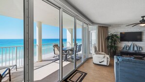 Ein geräumiger Balkon mit Meerblick, eine Sitzecke mit Tisch und Stühlen sowie ein Wohnzimmer mit Sofa und Fernseher.