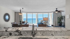 Ein geräumiger Wohnbereich mit großem Fenster zum Meer, eine Küche mit Marmorarbeitsplatte und einem Deckenventilator.