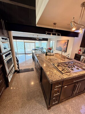 A modern kitchen with a large island, stainless steel appliances, and a view to a balcony overlooking water.