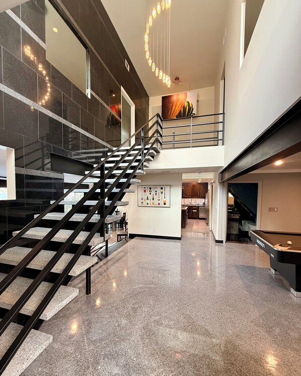 A modern interior with a spiral staircase, polished floors, and a billiards table.
