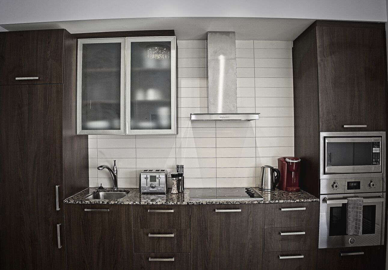 A modern kitchen with dark wood cabinets, a granite countertop, a double sink, a toaster, a kettle, and a built-in oven.