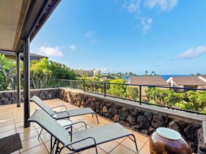 A balcony with two lounge chairs, a stone wall, and a view of the ocean and buildings. - Wailea Elua Village 307 | Wrap-Around Lanai, Seclusion & Steps to Ulua Beach (Wailea)