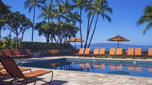 A poolside area with lounge chairs and umbrellas, palm trees, and a view of the ocean. - Wailea Elua Village 307 | Wrap-Around Lanai, Seclusion & Steps to Ulua Beach (Wailea)