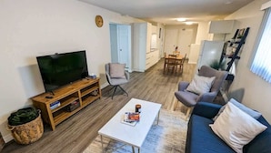 A living room with a TV, sofa, coffee table, and chairs. There is a dining area with a table and chairs in the background.