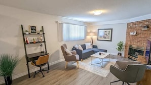 A living room with a sofa, coffee table, and chairs. There is a bookshelf with decorative items and a fireplace.