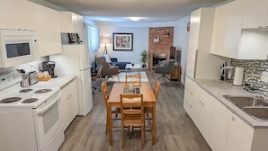 A compact kitchen with white cabinets, a microwave, stove, and a dining area with a wooden table and chairs.