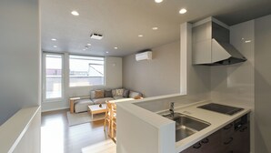 A modern kitchen with a built-in island, a dining area with a sofa and chairs, and a large window providing natural light. - Higashikawa Hinna (Higashikawa)