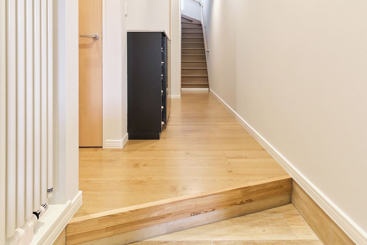 A narrow hallway with wooden flooring, a black cabinet, and a staircase at the end.