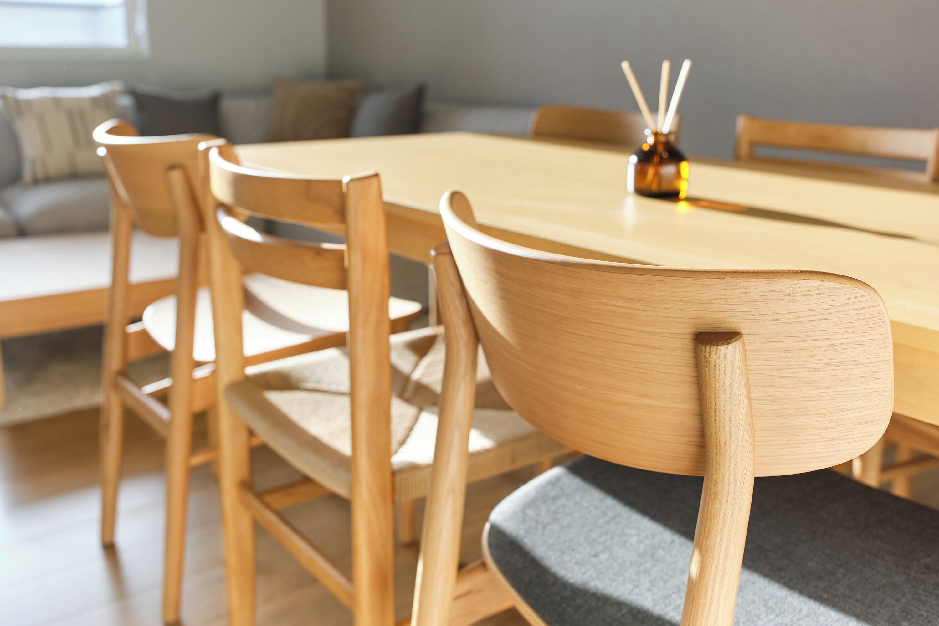 A dining area with a wooden table and chairs, a vase with candles, and a sofa in the background.