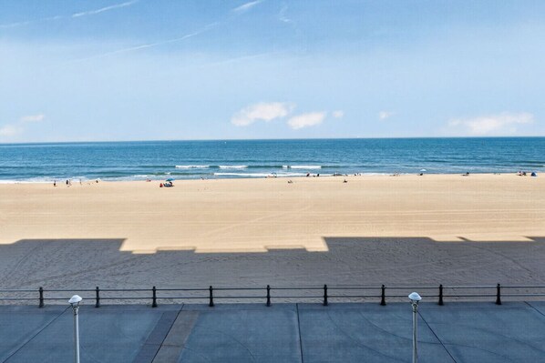 Ein Strand mit blauem Himmel, sandigem Ufer und einem Geländer im Vordergrund.