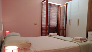 A bedroom with a bed, a nightstand, a lamp, a wardrobe, and a window with blinds. - Cozy Apartment Over the Sea, Villa Cecilia ap 2- two Hours Drive From Naples (Pisciotta)