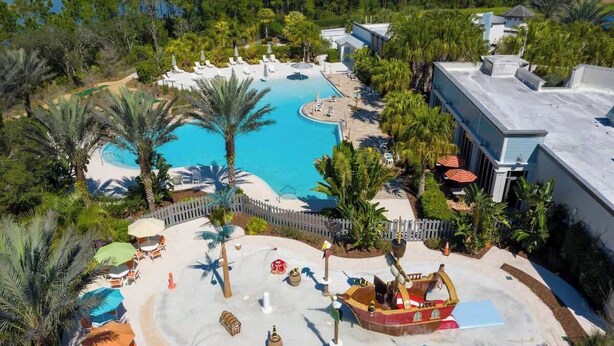 Un resort con una amplia piscina, palmeras y una zona de juegos con forma de barco.