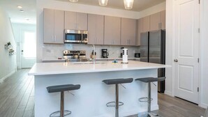 Una cocina moderna con una isla central, electrodomésticos de acero inoxidable e iluminación colgante.