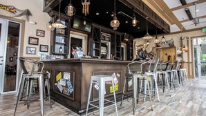 Una zona de bar con mostrador de madera, taburetes de metal e iluminación colgante.