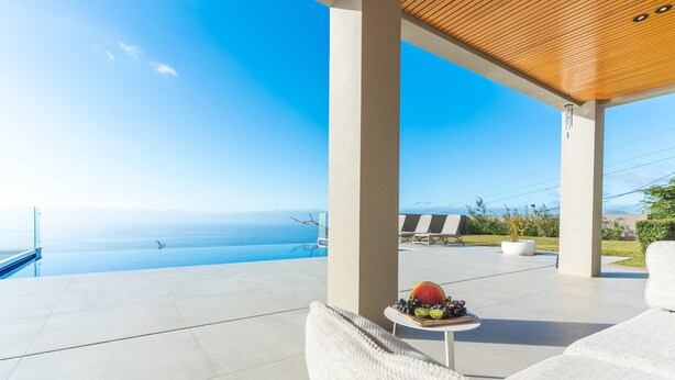 A modern outdoor seating area with a view of the ocean, a wooden ceiling, and a table with fruits. - Eco Monte by Atlantic Holiday (Funchal)